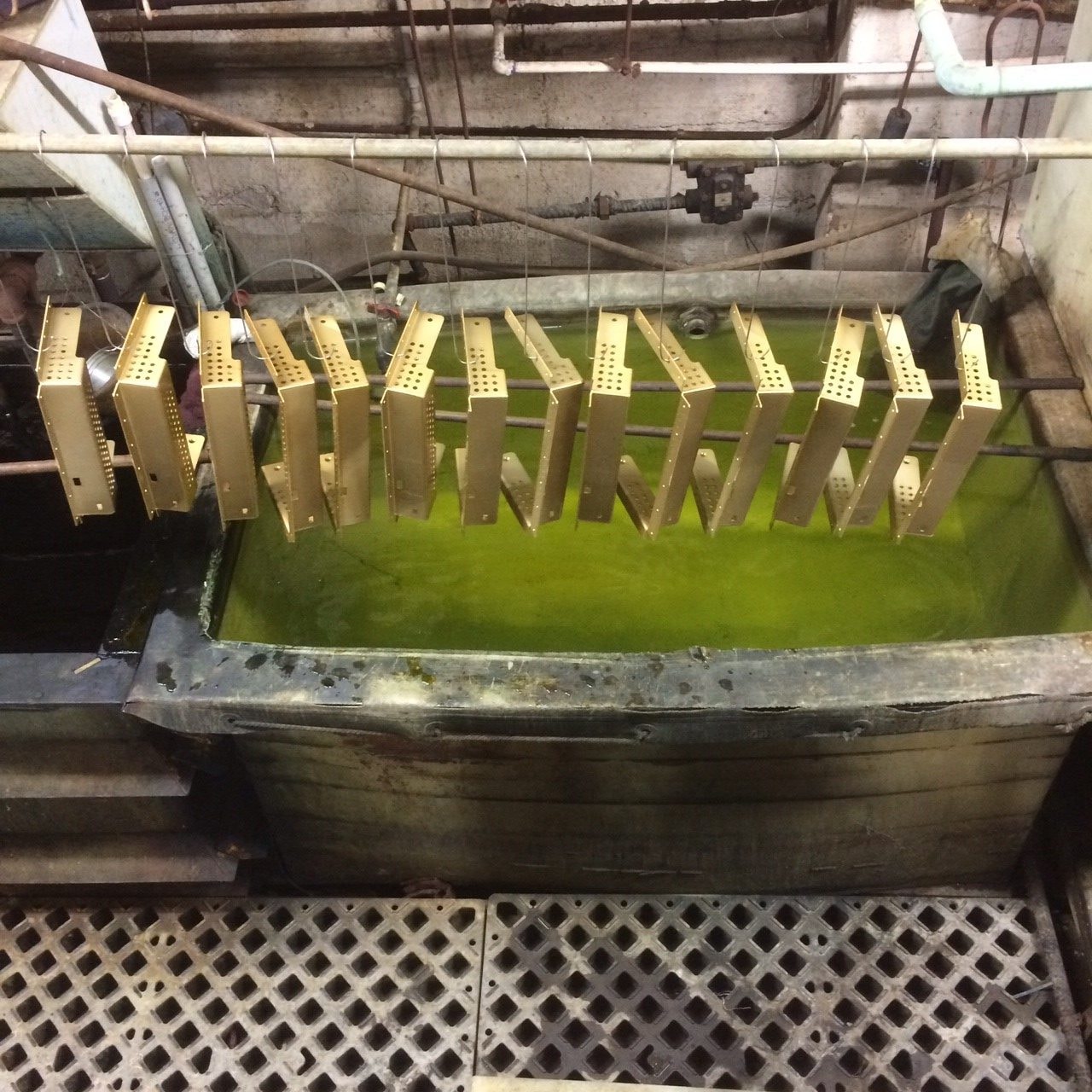 Gold-plated parts racked over a plating tank on the shop floor